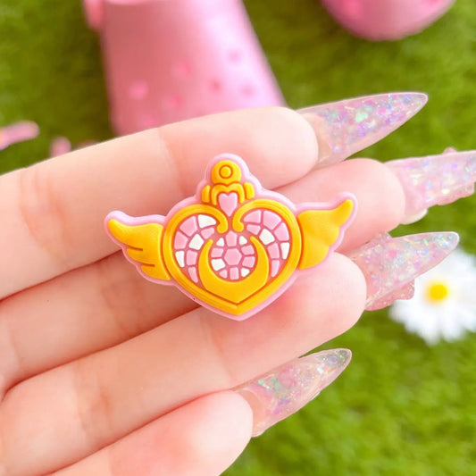 Hand holding a Sailor Moon inspired pink and yellow rubber shoe charm with a floral design on a green background.